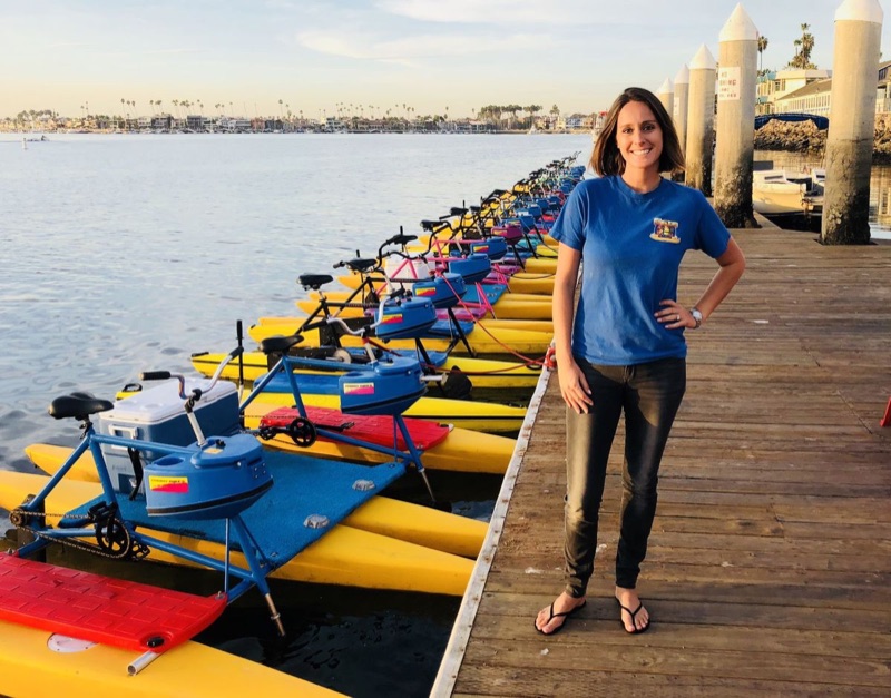 Melissa on the Long Beach Waterbikes dock on Alamitos Bay beside a long row of hydrobikes at golden hour