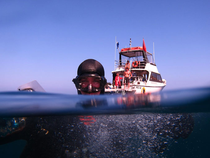 A scuba diver at the water surface with a Sundiver dive boat behind him