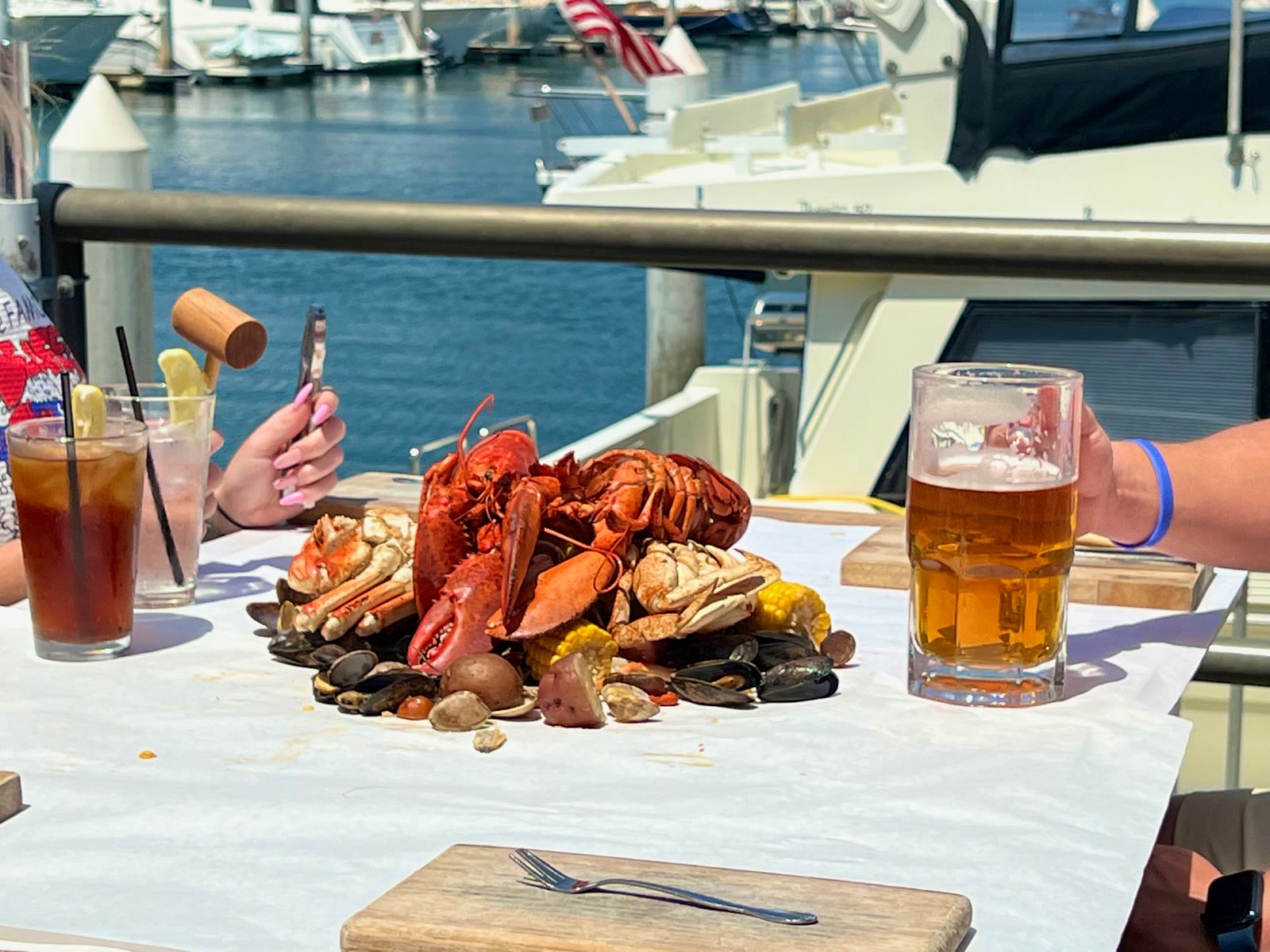 A Crab Pot Seafeast of crab, lobster and clams spread on a paper covered table with a beer and the marina behind