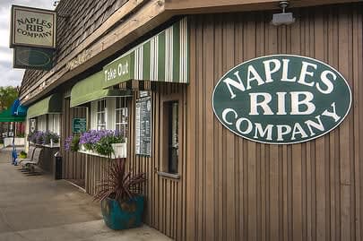 The front of Naples Rib Company on Second Street, with its oval green sign, Take Out awning and flower boxes
