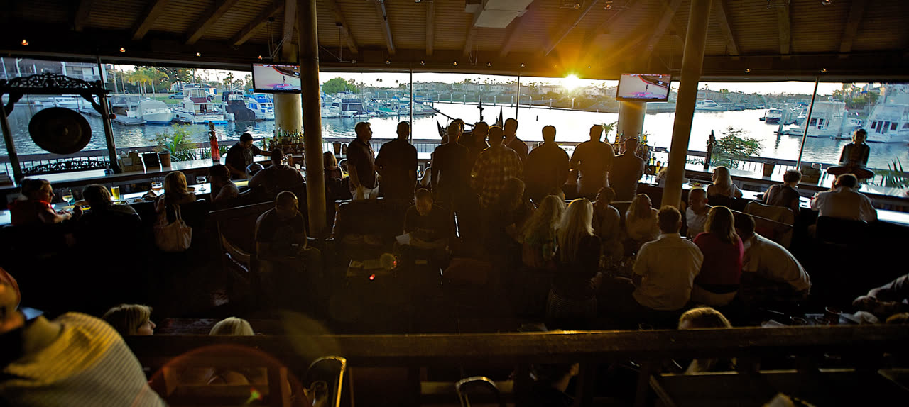 Sunset over the marina through Tantalum's wraparound windows, with guests at the bar and tables in silhouette